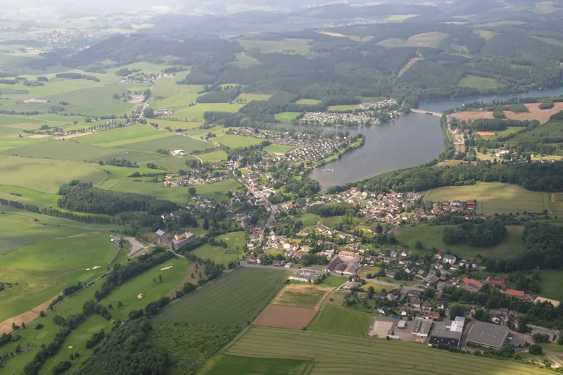 Der Sorpesee aus der Vogelperspektive, mit dem Dorf Amecke an seinem östlichen Ufer und den bewaldeten Hügeln des Sauerlands im Hintergrund