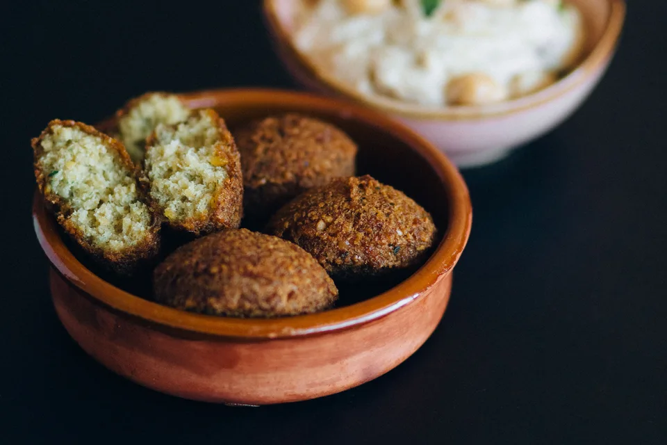 BookNoFees: Beispielfoto: Falafel-Bällchen, darunter ein aufgeschnittenes Stück, in einer Schüssel, dahinter Hummus