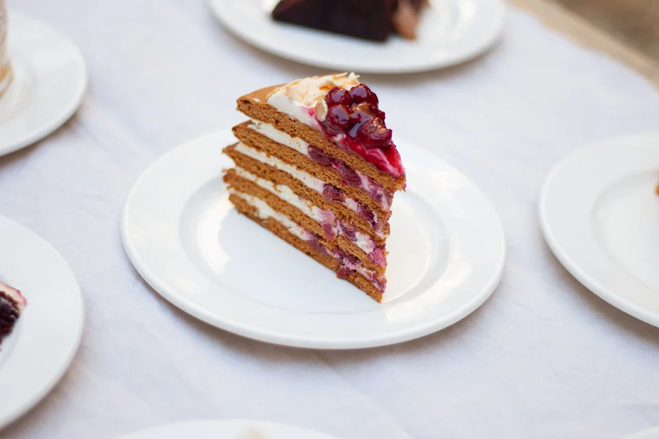 BookNoFees: Beispielfoto: Ein Stück Schichtkuchen mit Beeren als Garnitur auf einem weissen Teller