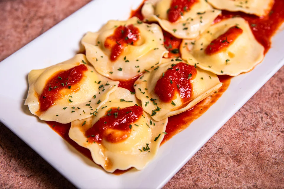 Beispielfoto: Ravioli mit Tomatensosse und Kräutern auf einem weissen Teller